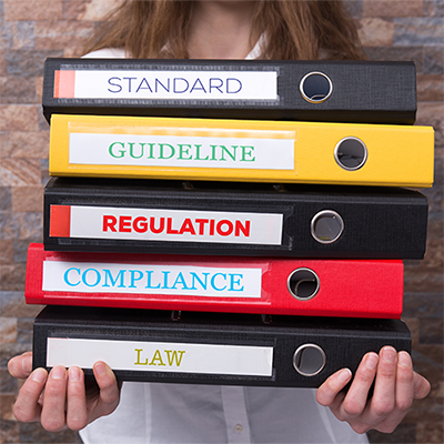Woman holding a stack of notebooks labelled: Standard, Guideline, Regulation, Compliance, and Law.