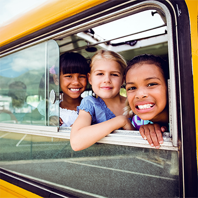 Smiling children looking out an open window on a school bus.